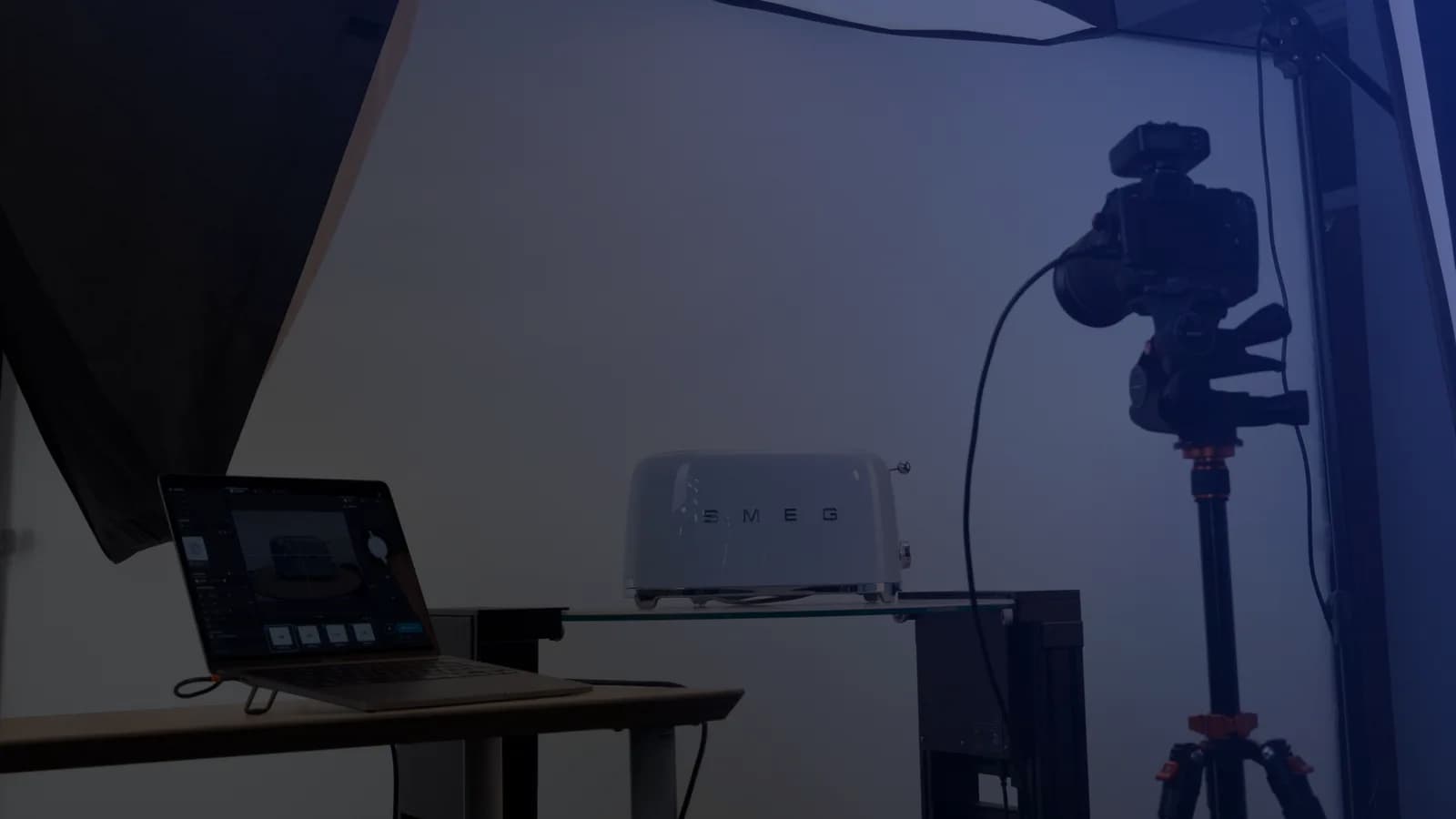 Tethered product photography setup - a laptop running capture software next to a camera on a tripod and a product on a glass shelf