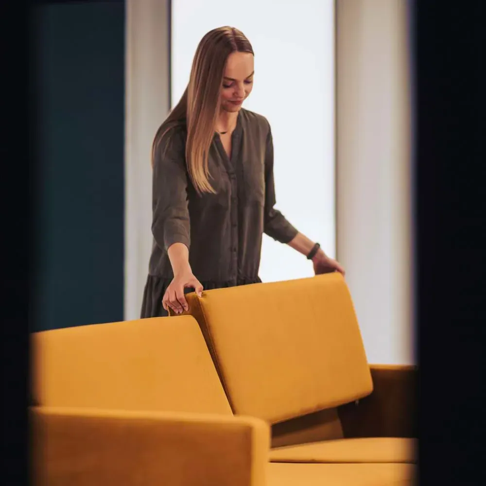 Woman arranging cushions on a yellow sofa for photography