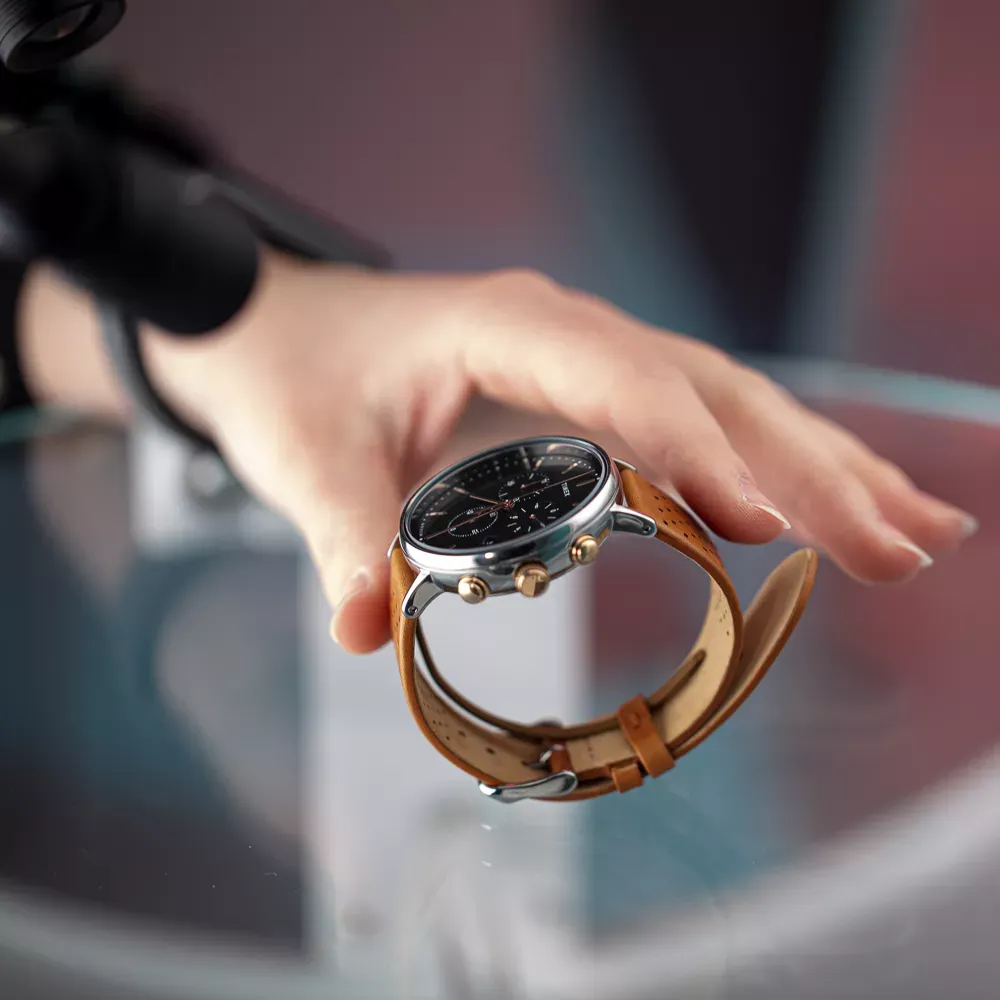 Hand positioning mens watch with brown leather strap on glass surface